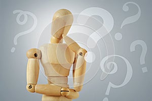 Wooden mannequin in thinking pose with quesion marks - Concept of question thinking and doubts