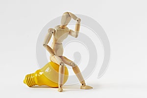 Wooden mannequin in thinking pose sitting on yellow light bulb - Concept of ideas and creative thinking