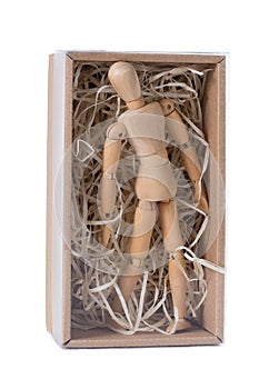 Wooden mannikin standing in closed cardboard box filled with wood shred. Concept of loneliness, isolation