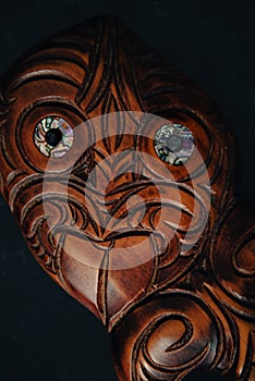 Wooden Maori Hei Tiki hand carved with paua shell eyes. New Zealand taonga. Closeup dark background.