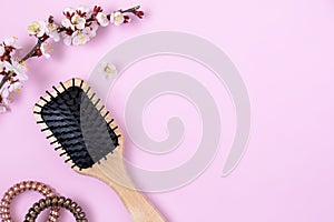 Wooden massage comb, spirals for hair and flowering apricot branch on pink background. beauty girl female concept