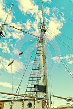 Wooden mast and ropes of sailboat, View of the ship`s masts from below, Detailed rigging without sails against blue sky.