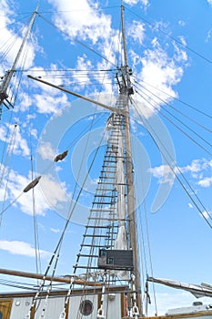 Wooden mast and ropes of sailboat, View of the ship`s masts from below, Detailed rigging without sails against blue sky.