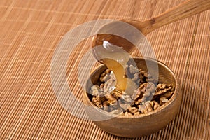 on a wooden mat, walnuts in a wooden bowl, honey is poured from a wooden spoon on top