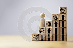 Wooden miniature figure standing on second step of staircase with dartboard and up arrow for continuous enhancement business