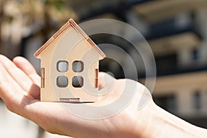 Wooden Model of a country house on a woman& x27;s palm with a residential building on the background