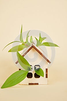 wooden model of a house on a beige background, eco house concept, green leaves and a small toy house