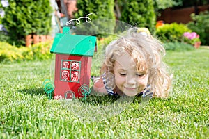 Wooden model of house and little blonde girl lying on grass