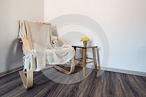 Wooden modern armchair cowered with cotton plaid and vase of yellow flowers on the small table near it