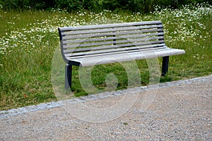 Wooden modern park bench with a metal relief structure on one leg stands in the park in rest areas and on paths made of a small