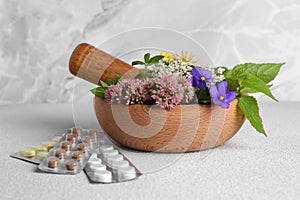 Wooden mortar with fresh herbs, flowers and pills on white table