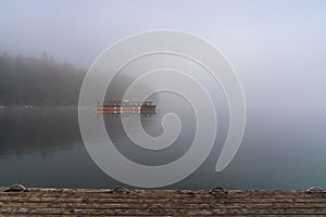 Wooden motorboat on a calm lake on a foggy morning with a wooden dock in the foreground