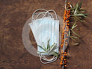 Wooden natural background with a medical protective mask with sea buckthorn branches, with berries. The idea of protecting against