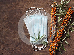 Wooden natural background with a medical protective mask with sea buckthorn branches, with berries. The idea of protecting against