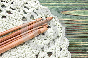 Wooden natural bamboo crochet hooks on the crochet doily and on the table. Creative work place for homemade crafts.