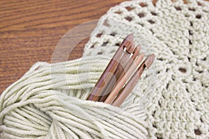 Wooden natural bamboo crochet hooks, doily and yarn ball on the table. Creative work place for homemade crafts. Top view.