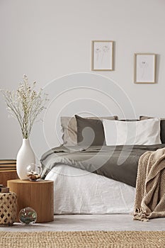 Wooden nightstand table next to king size bed with white and grey bedding in simple bedroom interior