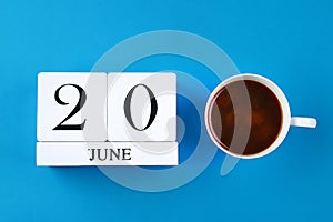 A wooden notebook with a date on June 20 and coffee mug on a blue pastel background. Father's Day.