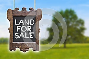 Wooden notice-board in a rural scene with Land for Sale text written on it against a blurred background - Real Estate concept