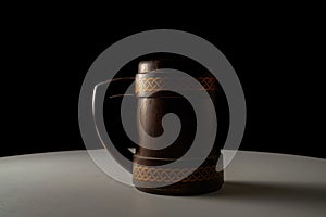 Wooden oak mug with a handle on white table isolated on black studio background. Brown mug with ornament in the dark