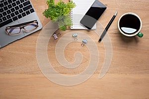 Wooden office desk table with smartphone with blank mock up screen, laptop computer, cup of black coffee and supplies. Top view