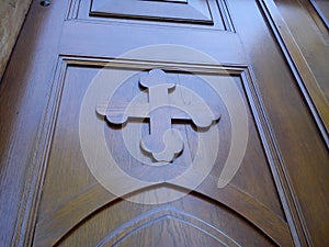 Wooden old church door. Carved wooden cross and varnished, smooth surface, shining in natural light