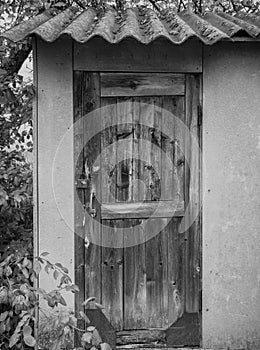 Wooden old door of a small house or barn. the roof is covered with slate. old rusty padlock. black and white