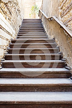 Wooden old weathered staircase going up with wooden handrail, between two stone bricks walls, in abandoned building