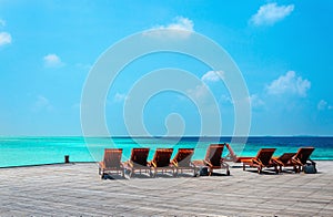 Wooden orange deck chairs on a pier on the background of the azure water, Indian Ocean, Maldives