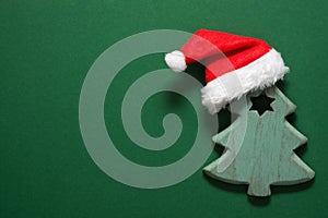 Wooden ornament Christmas tree with Santa Claus hat on top. Dark green background. New Year holiday greeting card poster banner