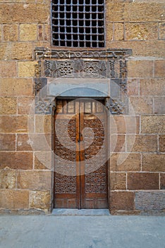 Wooden ornate door with geometrical engraved patterns on external old decorated bricks stone wall, Cairo, Egypt photo