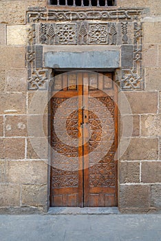 Wooden ornate door with geometrical engraved patterns on external old decorated bricks stone wall