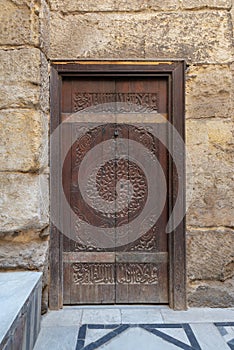 Wooden ornate door with geometrical engraved patterns on external old decorated bricks stone wall