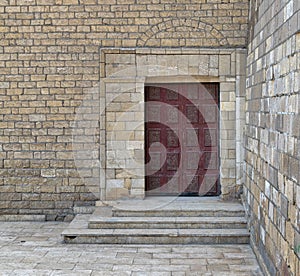 Wooden ornate engraved red door on bricks stone wall and deck stairs