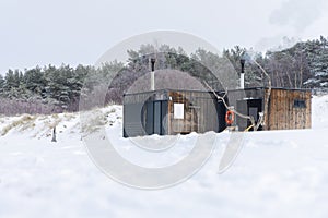 Wooden outdoor sauna with a smoke coming out of chimney on a beautiful cold snowy winter day at the Baltic sea.