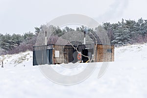 Wooden outdoor sauna with a smoke coming out of chimney on a beautiful cold snowy winter day at the Baltic sea.