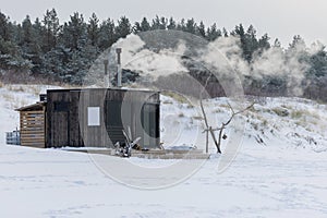 Wooden outdoor sauna with a smoke coming out of chimney on a beautiful cold snowy winter day at the Baltic sea.