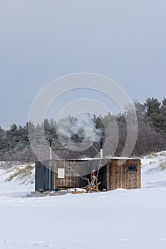 Wooden outdoor sauna with a smoke coming out of chimney on a beautiful cold snowy winter day at the Baltic sea. Well being and