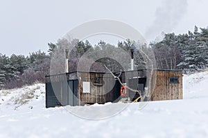 Wooden outdoor sauna with a smoke coming out of chimney on a beautiful cold snowy winter day at the Baltic sea. Well being and