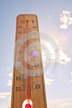 Wooden outdoor thermometer background scorching summer sun and blue sky.