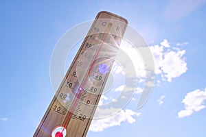 Wooden outdoor thermometer background scorching summer sun and blue sky.