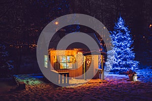 Wooden painted yellow private children play house in home garden, decorated with Christmas lights outdoors in cold night.