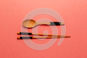 Wooden pairs of chopsticks and spoon on coral background. Top view. Flat lay. Copy space. Minimal style with colorful paper backdr