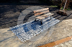 Wooden park bench with a metal frame in a park on a rectangle stone granite pavement. Design element around a grained gravel road