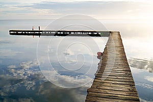 Wooden path access pontoon sunrise water reflection on Lake Hourtin in mirror image Gironde france