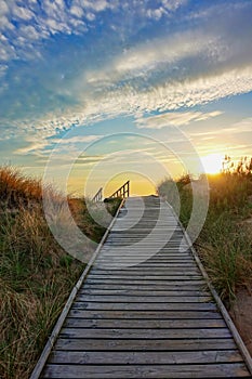 Wooden path at Baltic sea over sand dunes with ocean view, sunset summer evening