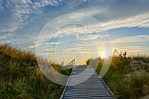 Wooden path at Baltic sea over sand dunes with ocean view, sunset summer evening