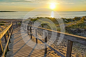 Wooden path at Baltic sea over sand dunes with ocean view, sunset summer evening