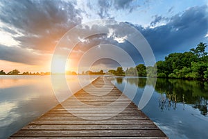 Wooden path bridge over lake at stormy dramatic sunset