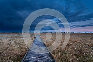 Wooden path on marsh at storm during sunset